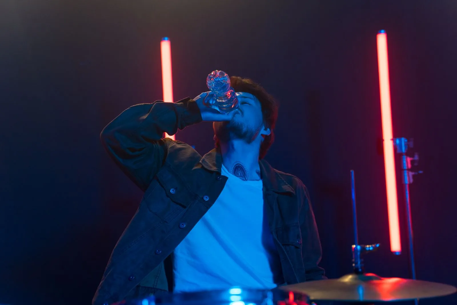 Man drinking water from a bottle in a neon-lit studio setting, capturing modern lifestyle.